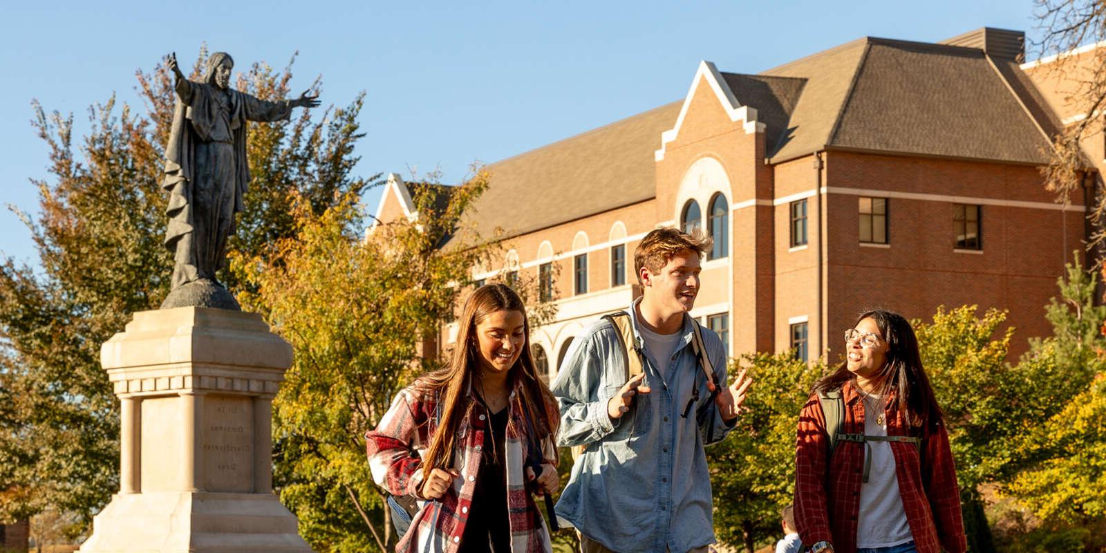 Students walking in Raven Memorial Park with the statue of the Sacred Heart of Jesus behind them